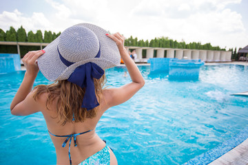 Beautiful young woman sitting on a pool with a hat