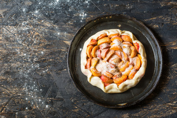  Homemade apricot galette made with fresh organic apricotes on wooden table, top view. Process of baking. Making dought. Hands with dought. Raw bakery. Open pie, apricot tart. Fruit bakery.