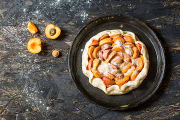  Homemade apricot galette made with fresh organic apricotes on wooden table, top view. Process of baking. Making dought. Hands with dought. Raw bakery. Open pie, apricot tart. Fruit bakery.