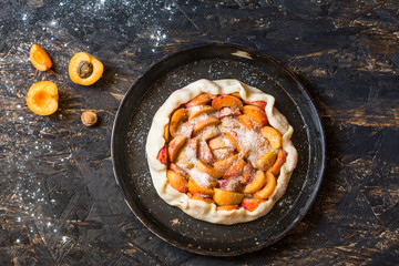  Homemade apricot galette made with fresh organic apricotes on wooden table, top view. Process of baking. Making dought. Hands with dought. Raw bakery. Open pie, apricot tart. Fruit bakery.
