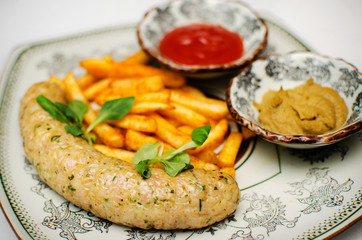Homemade sausage on a plate with fried potatoes, with sauces ketchup and mustard, decorated with green leaves.