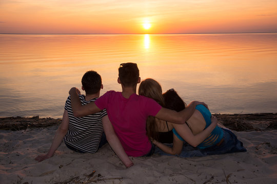 Four friends hugging on the beach and admiring the sunset