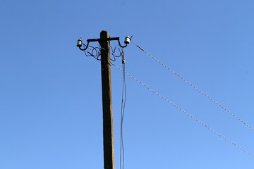 A post with broken electrical wires. On the electric column hang pieces of stained wires.