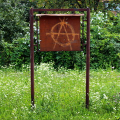 Anarchy graffiti painted on an old brown metal notice board (metal place for local for...