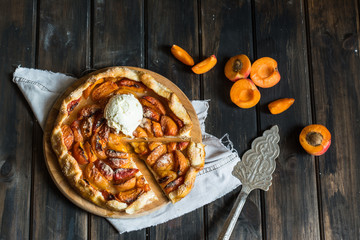  Homemade apricot galette made with fresh organic apricotes on wooden table, top view. Process of baking. Open pie, apricot tart. Fruit bakery. Cold Ice cream with warm pie.