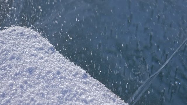 Snow is flying over surface of ice. Snowflakes fly on ice of Lake Baikal. Ice is very beautiful with unusual unique cracks. Snow sparkles and glows in red. Shooting slow motion 180fps. Picture at