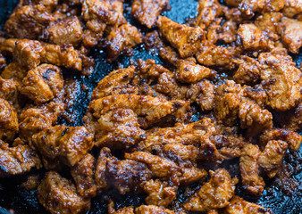 meat in marinade fried in a frying pan, many chicken pieces close-up