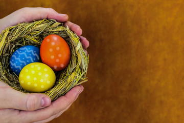 colorful eggs blue yellow decorated ornament in a woven straw nest present in hands with copy space