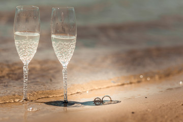 Beautiful high heel shoes with rings and glasses on sand. Beach wedding concept