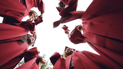 Slow motion low angle shot of graduates standing in circle throwing mortar-boards in the sky and laughing. Togetherness, friendship and modern lifestyle concept.