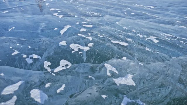 Snow is flying over surface of ice. Snowflakes fly on ice of Lake Baikal. Ice is very beautiful with unusual unique cracks. Snow sparkles and glows in red. Shooting slow motion 180fps. Picture at