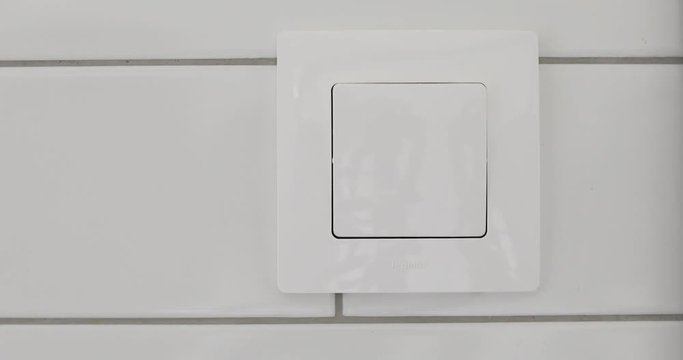 Female hand presses button of switch in bathroom close up. Hand with finger on light switch