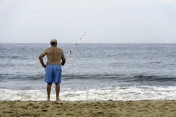 an elderly man is fishing on a sandy beach