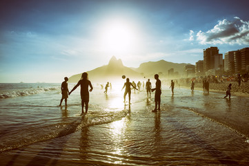 Distant sunset silhouettes playing keepy-uppie beach football on the sea shore in Ipanema Beach Rio...