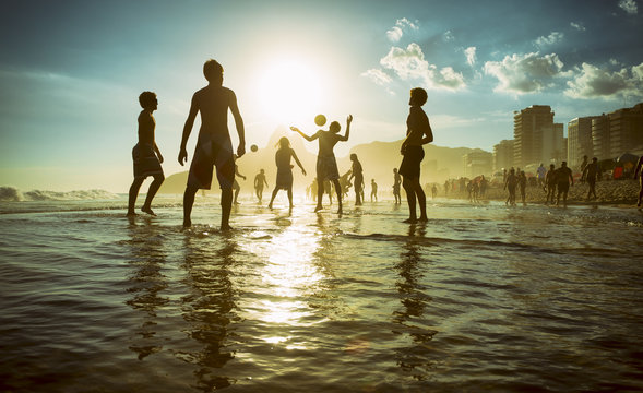 Distant sunset silhouettes playing keepy-uppie beach football on the sea shore in Ipanema Beach Rio de Janeiro Brazil