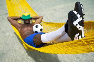 Brazilian soccer player in his boots relaxing in a beach hammock with a football resting in his lap