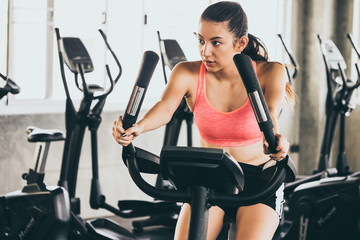 Fototapeta na wymiar Attractive young woman working out on exercise bike at the gym.