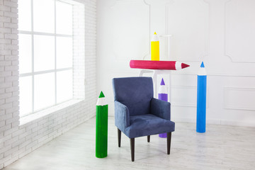 A white room with a blue chair and colored pencils in full height of a man