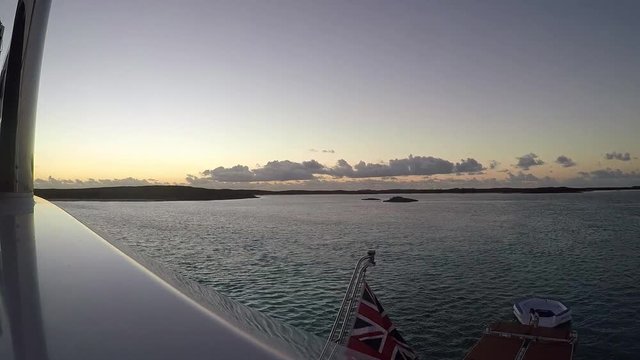Sunrise time-lapse from second floor yacht deck over ocean islands with waving flag.