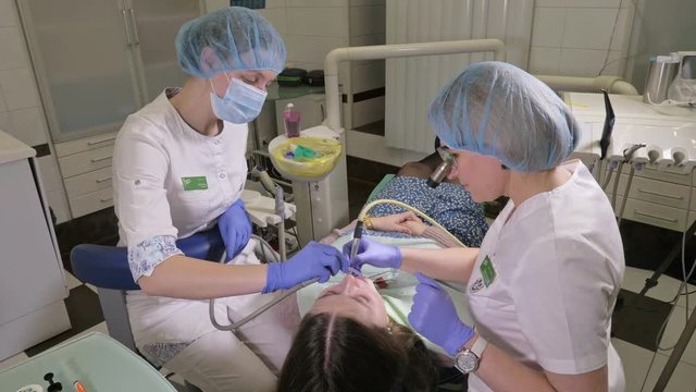 Woman at dentist clinic gets dental treatment to fill a cavity in a tooth. Dental restoration and composite material polymerization with UV light and laser. The doctor works with an assistant.