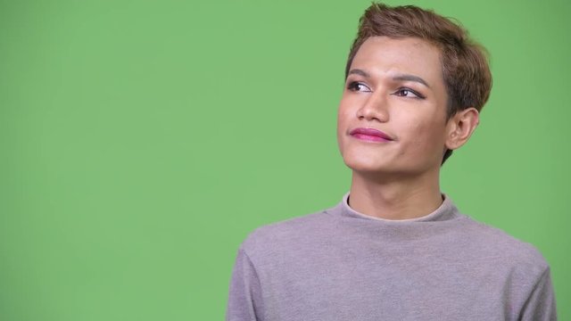 Happy young androgynous Asian man thinking