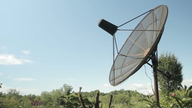 Metal Satellite dish aims at the sky under a clear blue sky in the middle of a green field