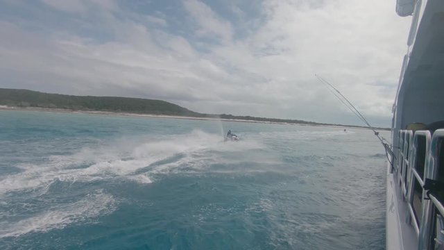 Jet ski races alongside large yacht between islands in the Exumas, Bahamas. Shot on GoPro action camera. Crashing waves behind boat.