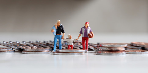 A family of four miniature people walking on coins. The concept of parenting and living expenses.