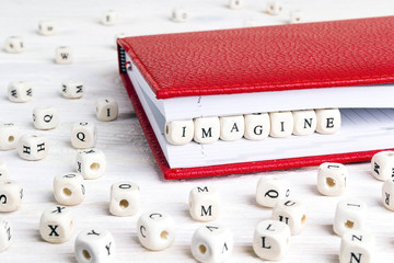Word Imagine written in wooden blocks in red notebook on white wooden table.