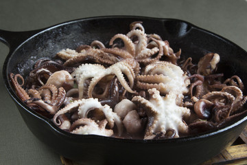 Mini octopus in the process of roasting on a cast iron pan