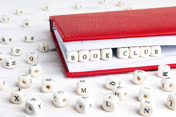Phrase Book club written in wooden blocks in red notebook on white wooden table.
