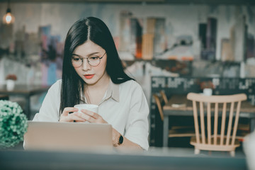 An Asian girl is freelancer woman, she is working by using the laptop computer and driking a cup of coffee on morning in a coffee shop or her office.