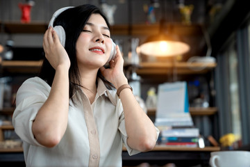 Close up the an Asian girl is freelancer woman, she is listening online music and using the laptop computer and driking a cup of coffee on morning in a coffee shop or her office.