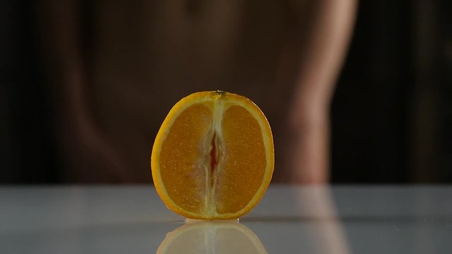 close-up half orange, woman takes off her panties on a dark background. imitation vagina. slow motion
