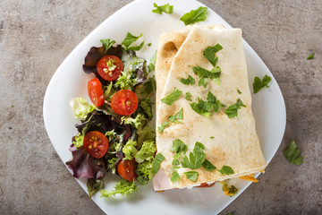 Sandwich or wrap filled with porkand beef meat and salami with salad on a white plate
