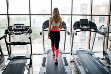 Horizontal shot of woman jogging on treadmill at health club. Female working out at a gym running...