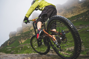 Legs of bicyclist and rear wheel close-up view of back mtb bike in mountains against background of...
