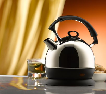 Electric kettle and tea glass on a table. Yellow curtain and brown wall in the background