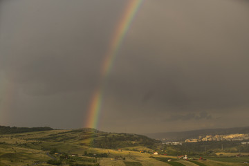 Beautiful rainbow over hills over the town and green hills