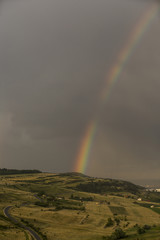 Beautiful rainbow over hills over the town and green hills