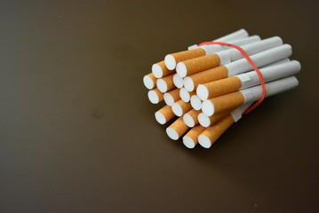 Cigarettes from the pack are fixed with a red rubber band on a brown matte background
