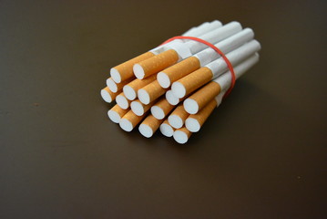Cigarettes from the pack are fixed with a red rubber band on a brown matte background