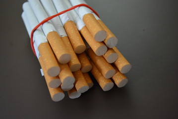Cigarettes from the pack are fixed with a red rubber band on a brown matte background
