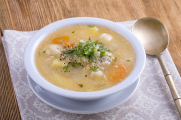 Fresh vegetable soup made of carrot, potato, cauliflower, parsley and rice in white plate,