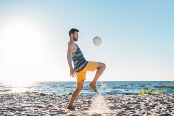handsome young man playing with ball on sandy beach