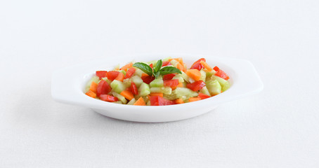 Tomato, cucumber and carrot pieces mixture, which is an healthy diet that might provide more nutrients than cooked vegetables and help in weight loss, with basil leaves topping.