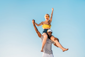 low angle view of happy young multiethnic couple having fun together against blue sky