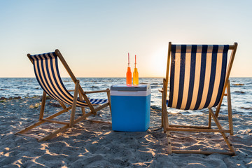 refreshing beverages on cooler and chaise lounges on sandy beach at sunset