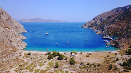 Naklejka premium Aerial birds eye view photo taken by drone of famous tropical rocky beach of Nannou with yachts docked and clear turquoise waters, Symi island, Dodecanese, Greece