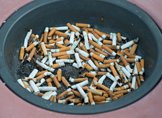 Black ashtray full of cigarette butts. Cigarette stubs.